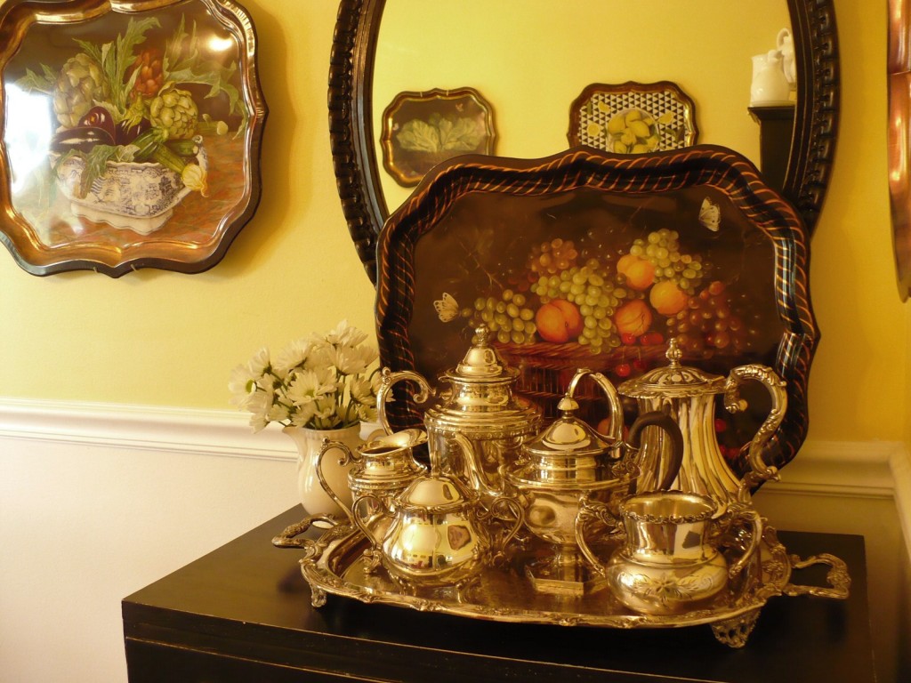 top of black bureau with polished silver teapots and tin tray