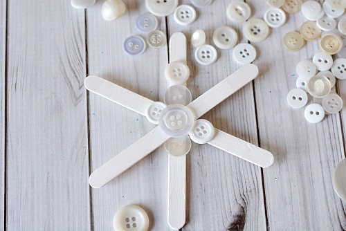 Popsicle Stick Button Sneeuwvlok - Dit zelfgemaakte kerstboomornament is zo leuk om te maken en gemakkelijk aan te passen!  Voeg dit jaar deze schattige DIY-ijslollyknop-sneeuwvlok toe aan je boom!  |  diy kerstornament, kerstknutselen, zelfgemaakte kerstornamentideeën